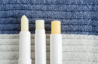 Three lip balms on the knitted background. Winter lip care sticks with beeswax, honey, panthenol and shea butter. Copy space.  clipart
