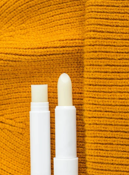 Two lip balms on the orange knitted background. Winter lip care sticks with beeswax, honey, panthenol and shea butter. Copy space.