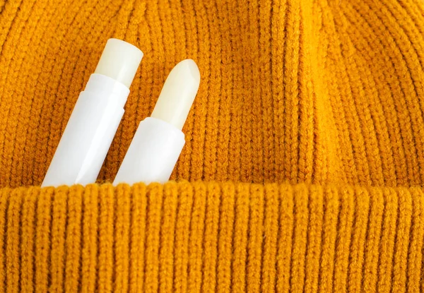 Two lip balms on the orange knitted background (pocket). Winter lip care sticks with beeswax, honey, panthenol and shea butter. Copy space.
