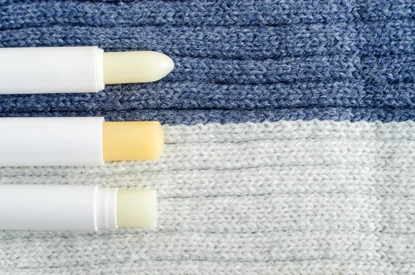 Three lip balms on the knitted background. Winter lip care sticks with beeswax, honey, panthenol and shea butter. Copy space.