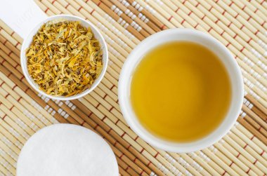 Doğal cilt bakımı ve tıbbi amaçlar için ev yapımı takvim tentürü (toner, infüzyon, decoction, yağ) olan küçük beyaz kase. Kuru kadife çiçekleri kapanıyor. On numara güzellik reçetesi. Üst görünüm  