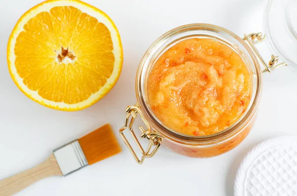 Homemade orange fruit facial mask (exfoliating sugar scrub) in the glass jar. Citrus DIY beauty treatment and spa recipe. Top view, copy space