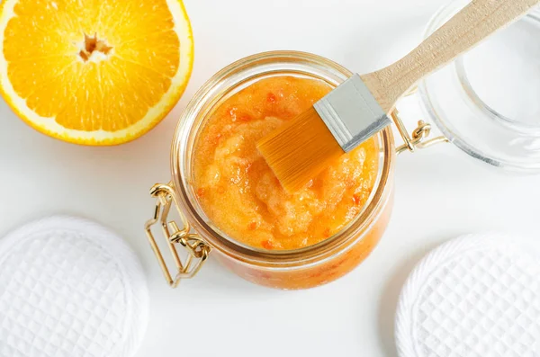 Homemade orange fruit facial mask (exfoliating sugar scrub) in the glass jar. Citrus DIY beauty treatment and spa recipe. Top view, copy space