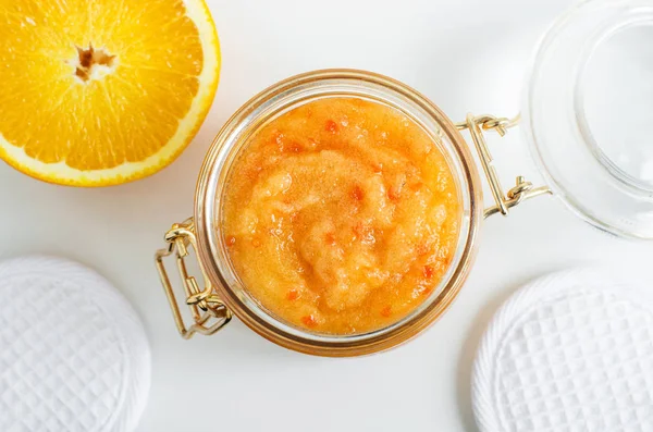 Homemade orange fruit facial mask (exfoliating sugar scrub) in the glass jar. Citrus DIY beauty treatment and spa recipe. Top view, copy space