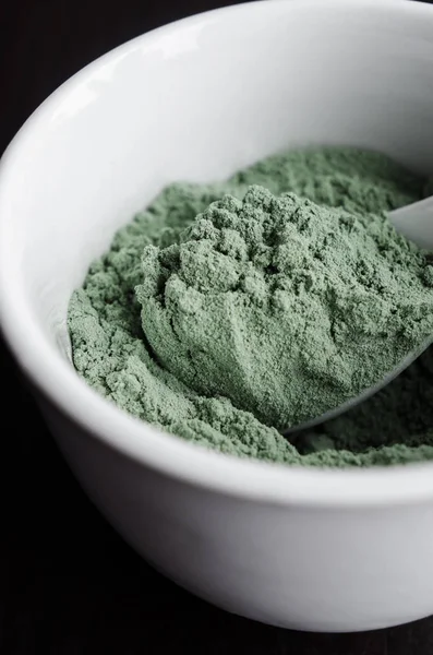 Green bentonite clay powder in the bowl. Diy facial mask and body wrap recipe. Dark background, clay texture close up, copy space