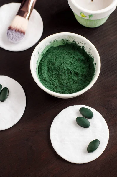 Spirulina powder in the small white bowl for preparing facial masks and exfoliating scrubs. Natural beauty treatment and spa recipe. Close up, top view, copy space — ストック写真