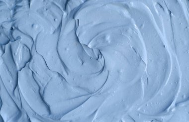 Açık mavi bentonit yüz kilini (maske, yüz kremi, vücut sargısı) kapat, seçici odaklanma. Fırça darbeleriyle soyut arkaplan.  