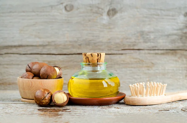 Vintage bottle with macadamia nut oil and wooden hair brush. Ingredients of homemade cosmetics - face and hair masks and moisturizers. Wooden background. Copy space. — Stock Photo, Image