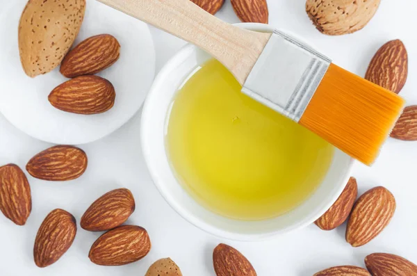 Pequeño tazón blanco con aceite de almendras para el cuidado natural de la piel y el cabello. Aceite limpiador ecológico, maquillaje removedor. Vista superior, espacio de copia . — Foto de Stock