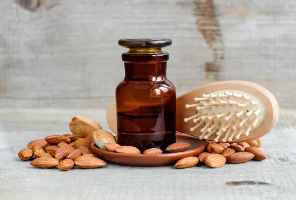 Botella de farmacia con aceite de almendras y cepillo de madera. Concepto natural de cuidado del cabello. Antiguo fondo de madera. Almendras cerca. Copiar espacio — Foto de Stock