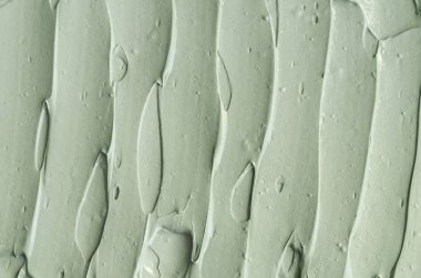 Gri bentonit yüz kilini (maske, yüz kremi, vücut ambalajı) kapat, seçici odaklanma. Fırça darbeleriyle soyut arkaplan.   