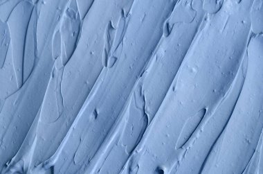 Açık mavi bentonit yüz kilini (maske, yüz kremi, vücut sargısı) kapat, seçici odaklanma. Fırça darbeleriyle soyut arkaplan.   