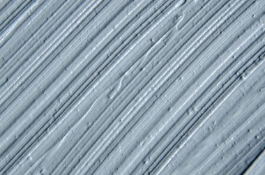 Gri bentonit yüz kilini (maske, yüz kremi, vücut ambalajı) kapat, seçici odaklanma. Fırça darbeleriyle soyut arkaplan.  