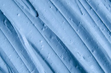 Açık mavi bentonit yüz kilini (maske, yüz kremi, vücut sargısı) kapat, seçici odaklanma. Fırça darbeleriyle soyut arkaplan.   