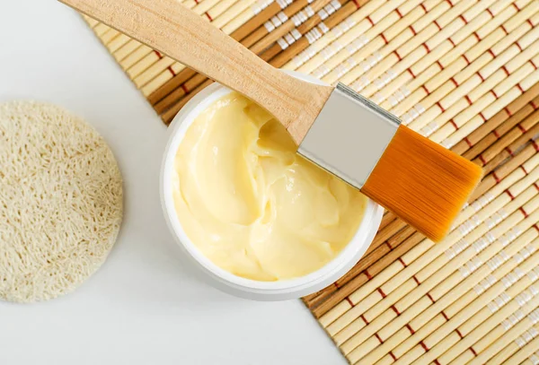 Yellow hair mask (banana face cream, shea butter facial mask, body butter) in the small white jar. Natural skin and hair care concept. Top view, copy space.