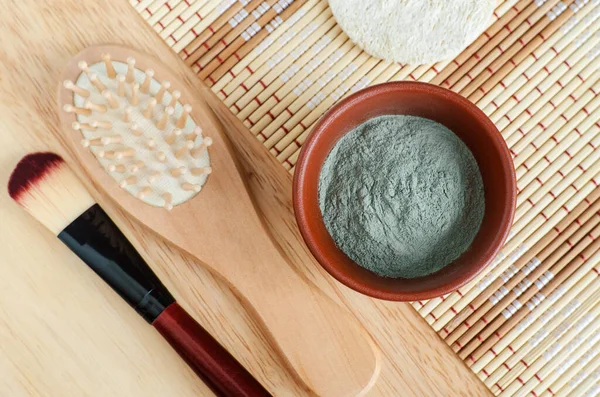 Green (blue) bentonite clay powder in the bowl, wooden hair brush and make-up brush. Clay texture close up. Diy facial or hair mask and body wrap recipe. Natural beauty treatment and spa. Top view, copy space