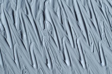 Gri bentonit yüz kilini (aljinat maskesi, yüz kremi, vücut sargısı) kapat, seçici odaklanma. Fırça darbeleriyle soyut arkaplan. 