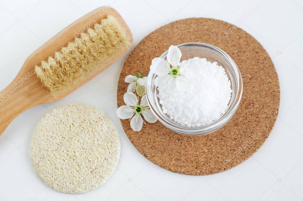 Small glass bowl with epsom bath salts (foot soak), wooden massage body brush and loofah sponge. Natural spa, beauty treatment, zero waste concept. Top view, copy space.