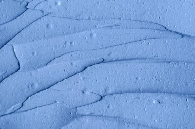 Açık mavi bentonit yüz kilini (aljinat maskesi, yüz kremi, vücut sargısı) kapat, seçici odaklanma. Fırça darbeleriyle soyut arkaplan. 