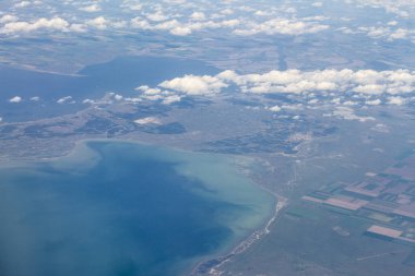 Bulutların arasından karaya ve denize giden bir uçağın en üst görüntüsü