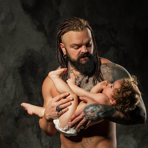 loving father shakes the baby in his arms. sporty brutal man with beard and tattoos holds in his arms a little curly-haired boy.
