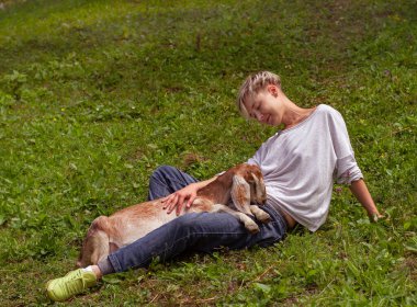 Mutlu neşeli kadın çimenlerin üzerinde küçük bir keçiyle yatıyor. Çiftlikteki insanların ve hayvanların dostluğu
