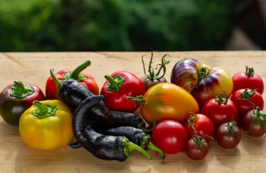 Ahşap bir tezgahın üzerinde farklı çeşitte biber ve domates var.