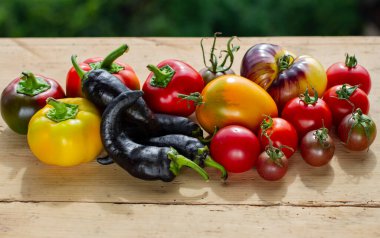 Tahta bir arka planda farklı türde biber ve domates var.