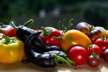 Ahşap bir tezgahın üzerinde farklı çeşitte biber ve domates var.