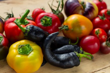 Tahta bir arka planda farklı türde biber ve domates var.