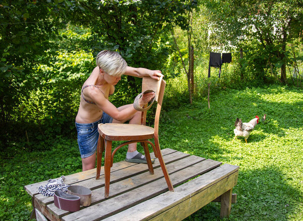 woman restorer works in the yard, sandpaper restores an old chair