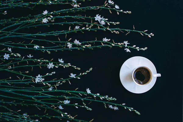 Coffee and flowers. Composition of wild spring tender flowers and cup of coffee on black background.  Spring coffee concept. Top view. Flat lay. Good morning.