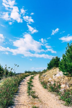 Dağ yolu. Güzel, parlak gökyüzü ile yürüyüş yolu. Aktif yaşam tarzı konsepti. Adriyatik kıyısında deniz manzaralı bir yolculuk. Aktif tatil konsepti. Kopyalama alanı olan bir arkaplan. Macera Zamanı.