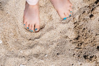 Çocuğun çıplak ayakları bahar tatilinde beyaz kumlu sahilde duruyor. Yaz tatili arka planında mesajlaşmak için yer var. Kumlu sahilde yürüyen küçük bir kız. Mutlu çocukluk. Mutlu ayak parmakları