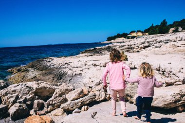 Çocuklar kayalara tırmanarak deniz kenarında yürüyorlar. Kardeş konsepti. Mutlu çocukluk kavramı. Tatil zamanı. Yaz geldi. Kopya alanı olan aile tatilleri arka planı.