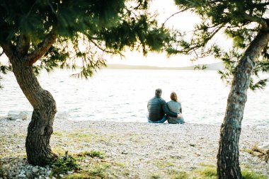 Genç mutlu evli çift deniz kenarında oturmuş günbatımını seyrediyor. Hayat tarzı balayı geçmişi, fotokopi alanı. Romantik bir kavram. Erkek ve kadın el ele tutuşuyor. Arkadan bak. Dijital detoks. Doğaya kaçıyorum. Çevrimdışı. Detoksifikasyon kavramı