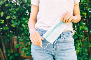 Cerrahi koruma maskesi yakın plan. Korona virüsü salgını sırasında kendini koruyan bej tişört ve kot pantolon giyen bir kadın. Metin için yeri olan Covid-19 pandemik arkaplan.