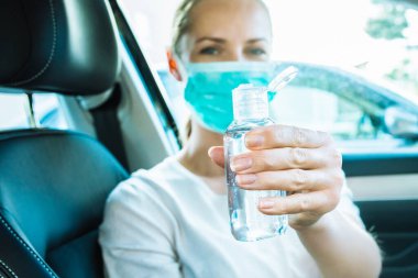 El dezenfektanı. Koruyucu cerrahi maske takan mutlu bir kadın arabaya biniyor ve virüse karşı ellerini temizlemek için el dezenfektanı veriyor. Coronavirus salgını. Covid-19 yeni bir hayat