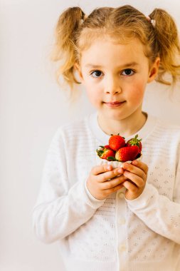 Güzel sarışın çocuk beyaz arka planda biyolojik çilek yiyor ve mesaj yazıyor. Pozitif arka plan. Yavaş yaşam konsepti. Bahar arka planı. Fırsatı kaçırmanın keyfi. Dikey yaşam tarzı portresi