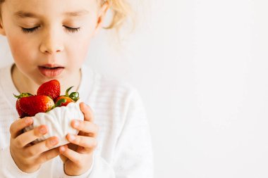 Çilekli. Küçük mutlu bir kız elinde organik çilekleri fotokopi odasıyla beyaz arka planda yiyor. Mevsimlik ev yapımı çilek yiyen çocuk. Çilek kokan çocuk..