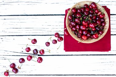 Beyaz kırsal arka planda dokuma kabında taze kiraz ve yeşil yaprakların yaratıcı düzeni ve metin için boş alan. Bahar geldi. Yaz tatili. Sağlıklı çerez