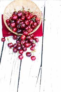 Beyaz kırsal arka planda dokuma kabında taze kiraz ve yeşil yaprakların yaratıcı düzeni ve metin için boş alan. Bahar geldi. Yaz tatili. Sağlıklı çerez