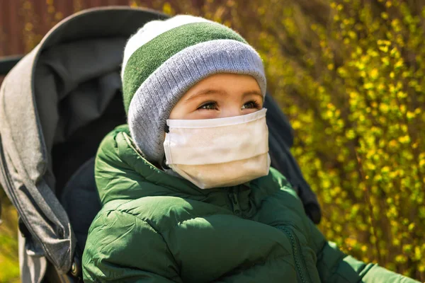 Parkta bebek arabasında maske takmış gülen küçük bir çocuk.