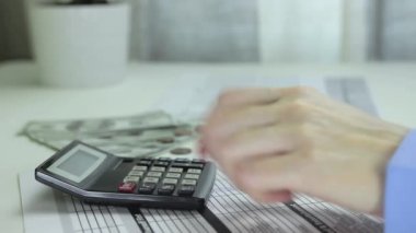 Kadın hesap makinesi kullanıyor ve veri tablosuna kalemle hesaplamalar yazıyor.