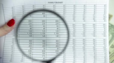 Kadın eli, aile bütçe tablosunun üzerinde büyüteç taşıyor. Gider analizi