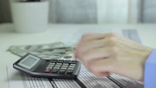Kvinna använder en miniräknare och skriver beräkningar med en penna i en datatabell — Stockvideo