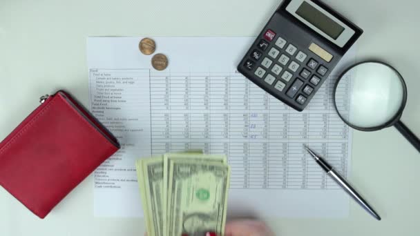 Žena počítá hotovost přes bílý stůl, na kterém leží peněženka, kalkulačka, lupa — Stock video
