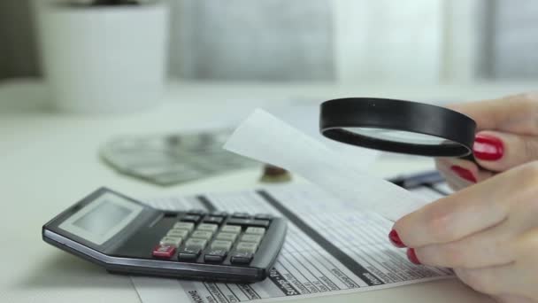Kvinna med förstoringsglas kontrollerar ett kvitto och skriver kostnaderna i tabellen — Stockvideo