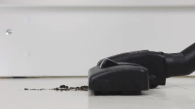 Elektrik süpürgesinin beyaz zemindeki toprağı temizlerken yakın plan görüntüsü.