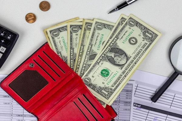 Beyaz masasında dolar banknotları olan kırmızı deri cüzdan.